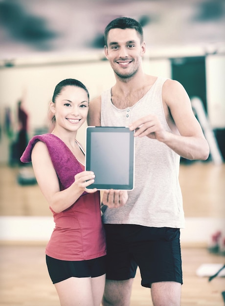 concepto de fitness, deporte, entrenamiento, gimnasio y estilo de vida: dos personas sonrientes que muestran la pantalla en blanco de la tableta