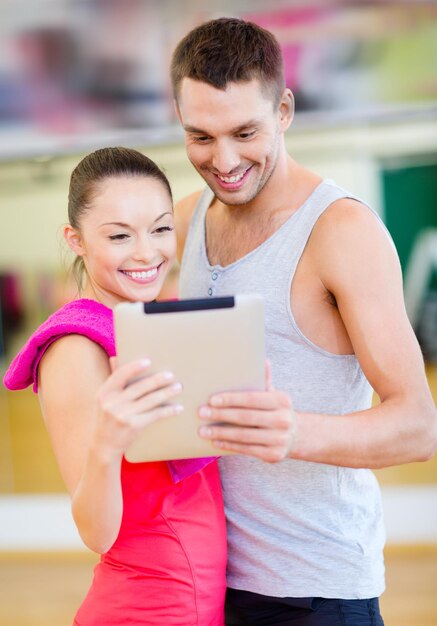 concepto de fitness, deporte, entrenamiento, gimnasio y estilo de vida: dos personas sonrientes con tablet pc en el gimnasio