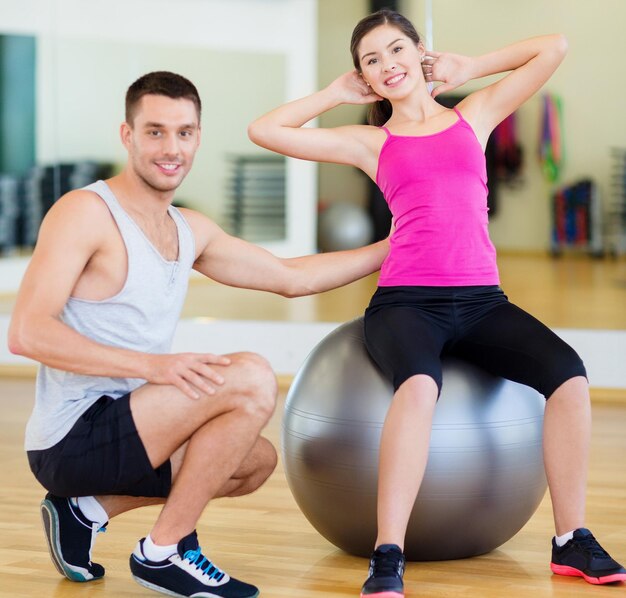 concepto de fitness, deporte, entrenamiento, gimnasio y estilo de vida - entrenador masculino con mujer haciendo abdominales con la pelota