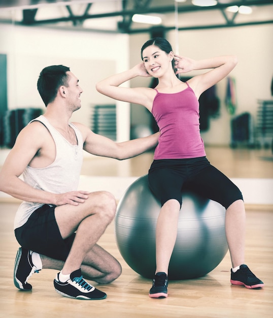 concepto de fitness, deporte, entrenamiento, gimnasio y estilo de vida - entrenador masculino con mujer haciendo abdominales con la pelota