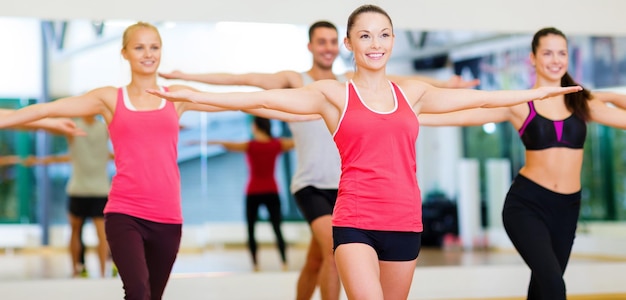 concepto de fitness, deporte, entrenamiento, gimnasio y estilo de vida - grupo de personas sonrientes haciendo ejercicio en el gimnasio