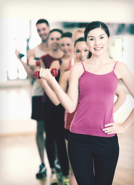 concepto de fitness, deporte, entrenamiento, gimnasio y estilo de vida - grupo de personas sonrientes levantando pesas en el gimnasio