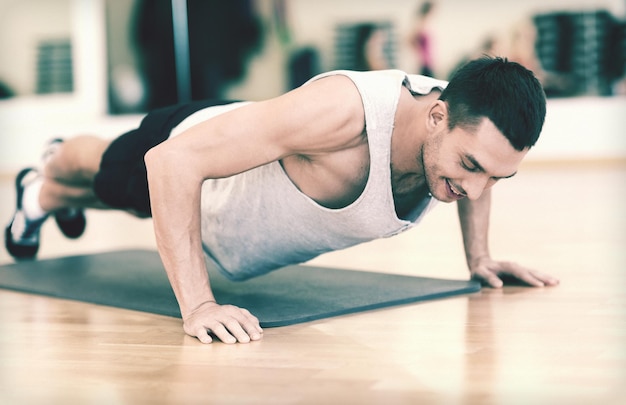 concepto de fitness, deporte, entrenamiento, gimnasio y estilo de vida - hombre sonriente haciendo flexiones en el gimnasio