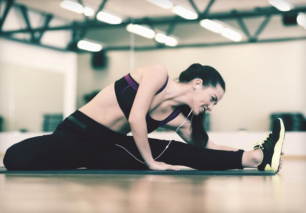 concepto de fitness, deporte, entrenamiento, gimnasio y estilo de vida - mujer sonriente que se extiende sobre una colchoneta en el gimnasio