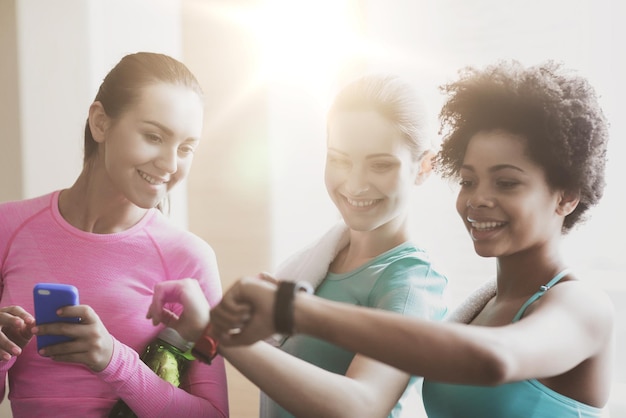 concepto de fitness, deporte, entrenamiento, gimnasio y estilo de vida - mujeres felices mostrando el tiempo en el reloj de pulsera en el gimnasio