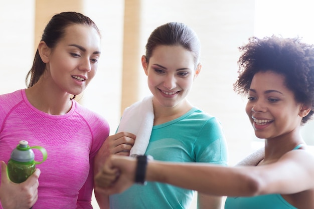 concepto de fitness, deporte, entrenamiento, gimnasio y estilo de vida - mujeres felices mostrando el tiempo en el reloj de pulsera en el gimnasio