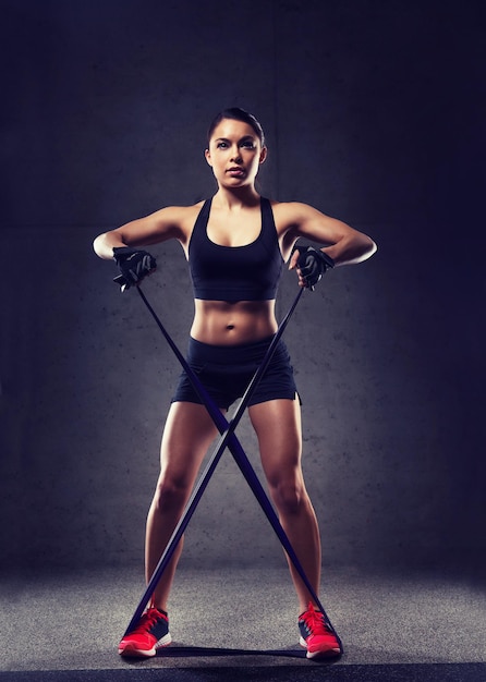 Concepto de fitness, deporte, entrenamiento, personas y estilo de vida: mujer haciendo ejercicios con expansor o banda de resistencia en el gimnasio