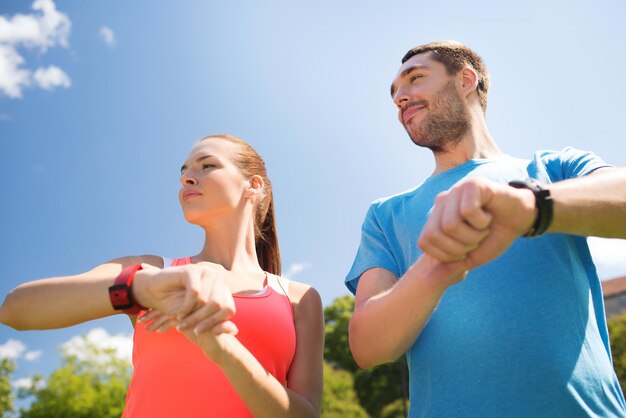 concepto de fitness, deporte, entrenamiento, tecnología y estilo de vida - dos personas sonrientes con relojes de frecuencia cardíaca al aire libre