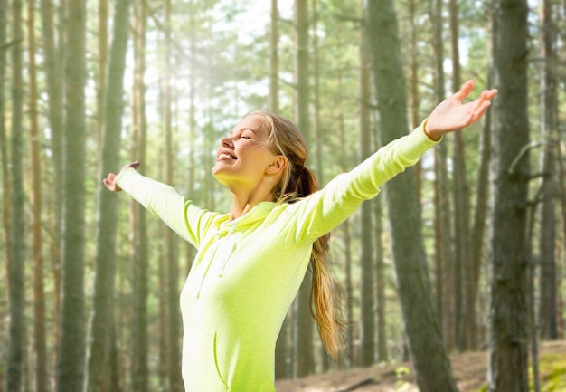 concepto de fitness, deporte, felicidad y personas - mujer feliz levantando la mano sobre el fondo del bosque