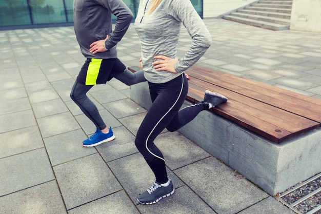 concepto de fitness, deporte, gente, ejercicio y estilo de vida - cerca de una pareja haciendo ejercicio de estocada en la calle de la ciudad