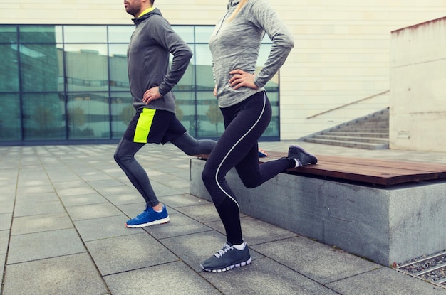 concepto de fitness, deporte, gente, ejercicio y estilo de vida - cerca de una pareja haciendo ejercicio de estocada en la calle de la ciudad