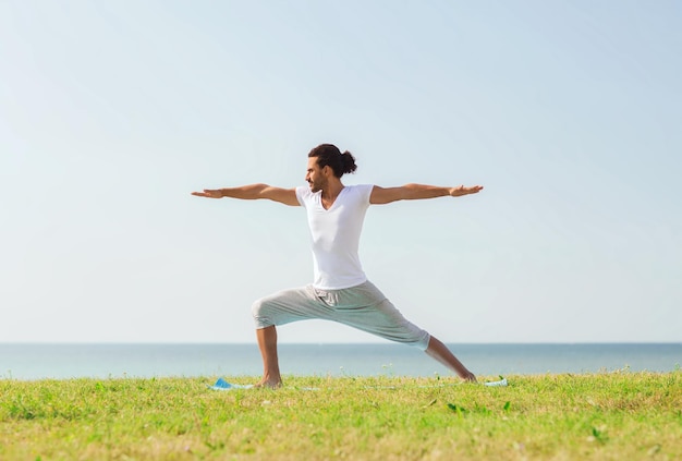 concepto de fitness, deporte, gente y estilo de vida - hombre sonriente haciendo ejercicios de yoga al aire libre