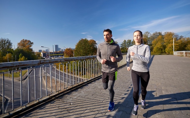 concepto de fitness, deporte, gente y estilo de vida - pareja feliz corriendo al aire libre