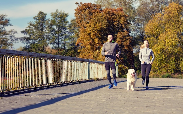 concepto de fitness, deporte, gente y estilo de vida - pareja feliz con perro corriendo al aire libre