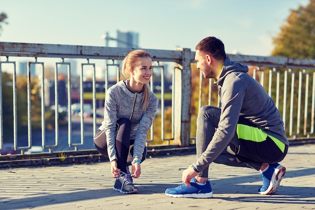 concepto de fitness, deporte, gente y estilo de vida - pareja sonriente atando cordones de zapatos al aire libre