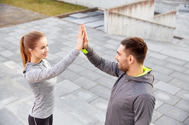 concepto de fitness, deporte, gente y gestos - pareja sonriente haciendo chocar los cinco en la calle de la ciudad