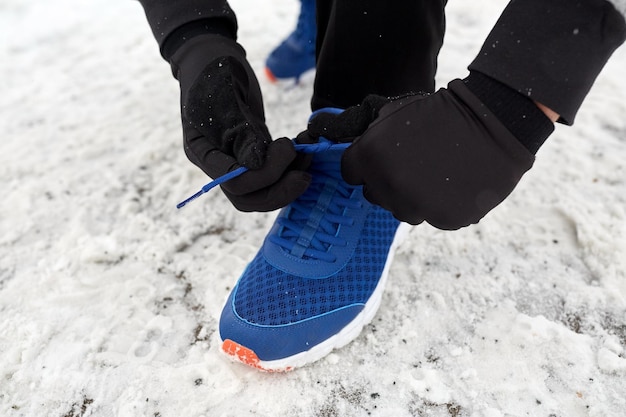 concepto de fitness, deporte, gente, ropa deportiva y calzado - cierre del pie y las manos del hombre atando cordones de zapatos en invierno al aire libre