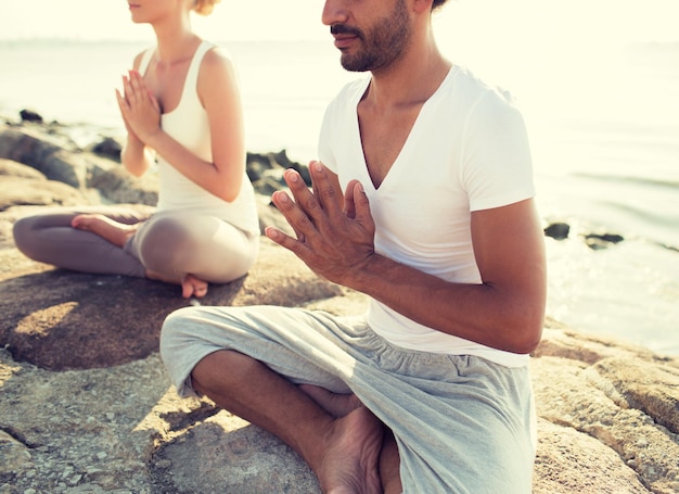 concepto de fitness, deporte, personas y estilo de vida - cerca de una pareja haciendo ejercicios de yoga sentados en el muelle al aire libre