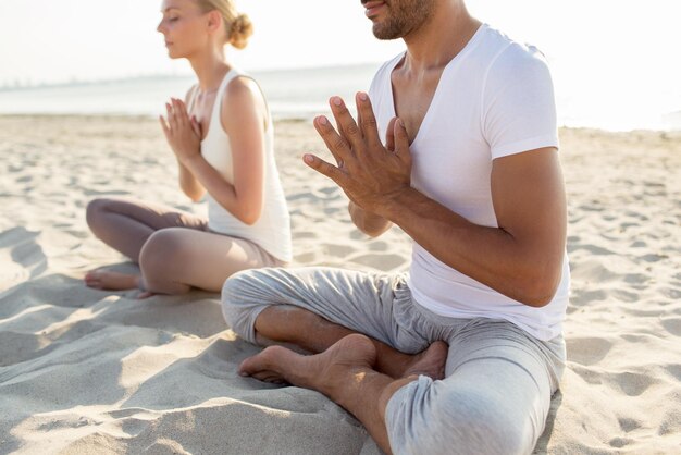 concepto de fitness, deporte, personas y estilo de vida - cerca de una pareja haciendo ejercicios de yoga sentados en el muelle al aire libre