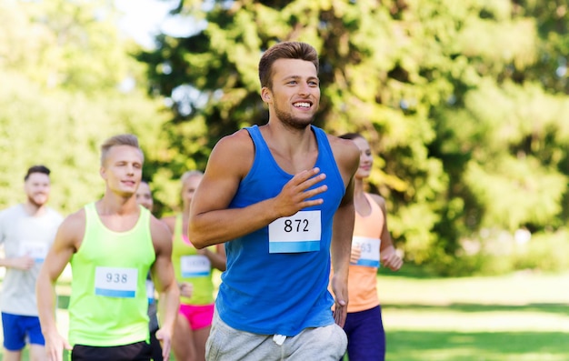 concepto de fitness, deporte, raza y estilo de vida saludable - grupo de amigos adolescentes felices o deportistas corriendo maratón con números de placa al aire libre