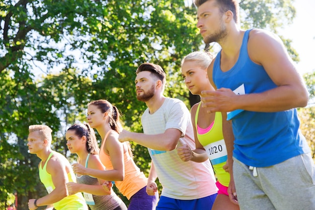 concepto de fitness, deporte, raza y estilo de vida saludable - grupo de amigos adolescentes o deportistas con números de placa al comienzo de la carrera de maratón al aire libre