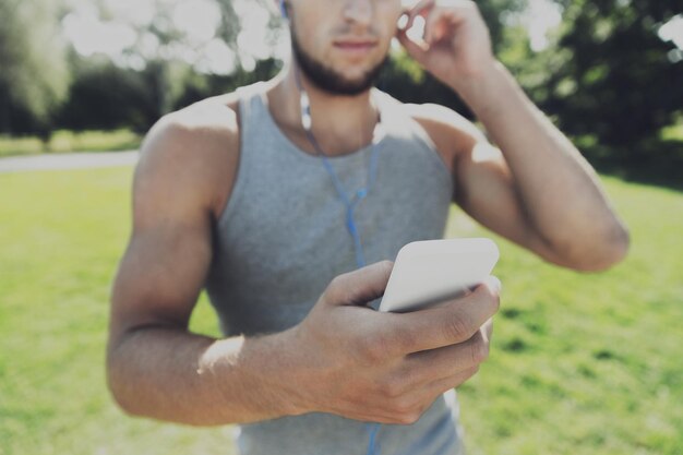 concepto de fitness, deporte, tecnología y estilo de vida - cerca de un joven con smartphone y auriculares escuchando música en el parque de verano