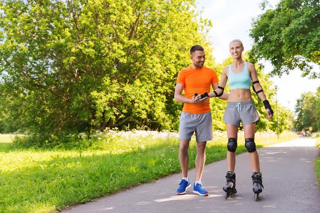 concepto de fitness, deporte, verano y estilo de vida saludable - pareja feliz con patines montando al aire libre