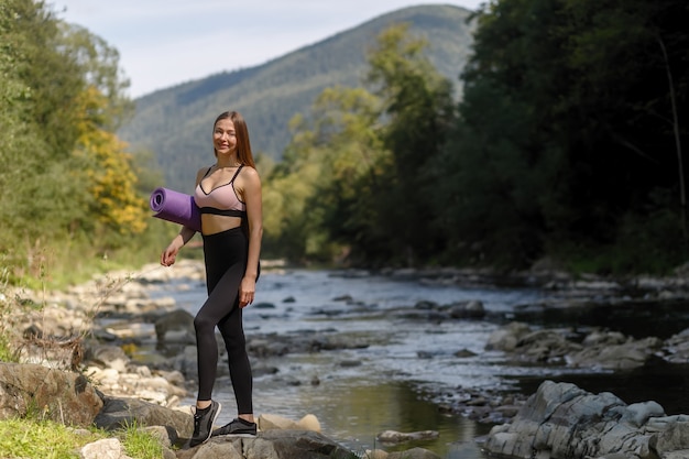 Concepto de fitness, deportes, yoga y estilo de vida saludable - mujer joven con cuerpo delgado y saludable de pie con estera de yoga