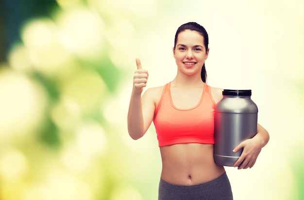 concepto de fitness y dieta - adolescente sonriente con tarro de proteína mostrando los pulgares hacia arriba