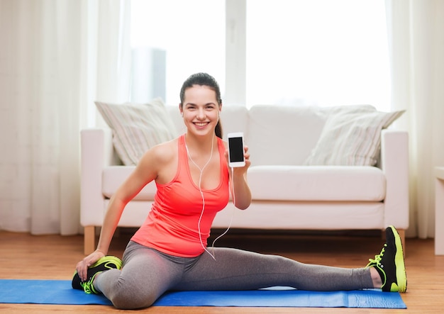 concepto de fitness, hogar, tecnología y dieta - adolescente sonriente estirando en el suelo con smartphone y auriculares en casa