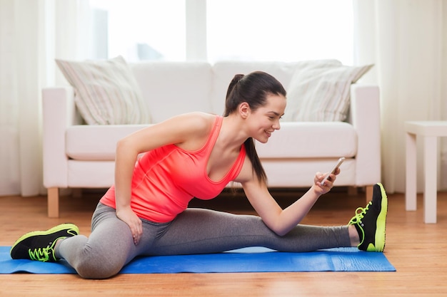 concepto de fitness, hogar, tecnología y dieta - adolescente sonriente estirando en el suelo con smartphone en casa