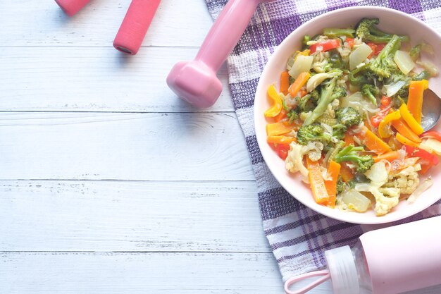 Foto concepto de fitness con mancuernas, verduras frescas y cinta métrica en rosa