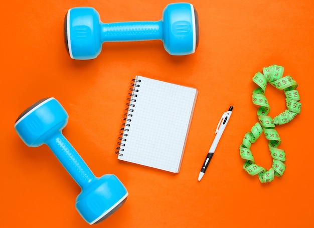 Concepto de fitness con pesas de plástico azul, bloc de notas y bolígrafo