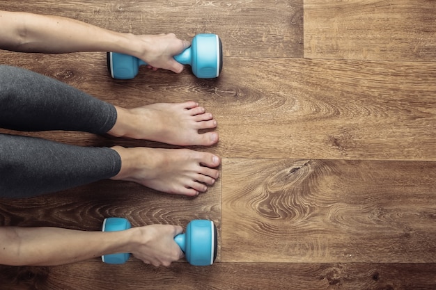 Concepto de fitness. Piernas femeninas en leggings y pies descalzos se sienta en el suelo con mancuernas.