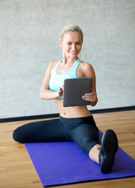 concepto de fitness, tecnología y deporte - mujer sonriente con tablet pc sentada en el gimnasio