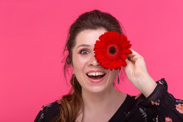 Concepto de flores, emociones y personas - la mujer cerró los ojos con gerbera en la pared rosa