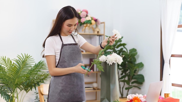 Concepto de floristería Floristería femenina corta el tallo de crisantemo con una tijera para hacer un ramo de flores en la tienda