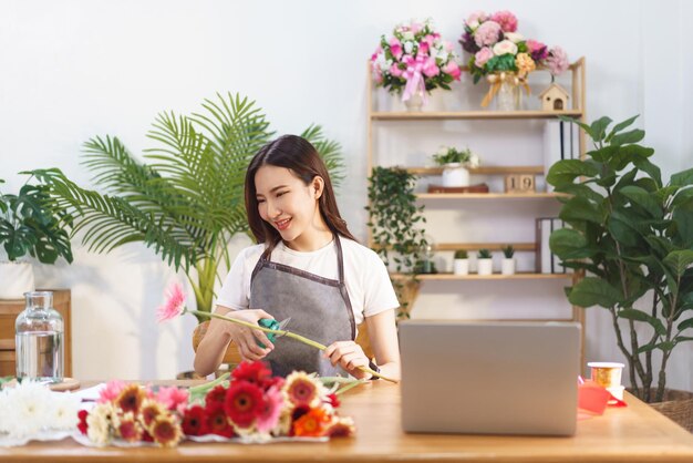 Concepto de floristería Floristería femenina cortando gerbera con tijera preparándose para hacer jarrón de flores en la tienda