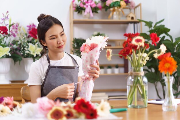 Concepto de floristería Sonrisa de floristería femenina y sosteniendo un colorido ramo de flores con papel y lazo de cinta