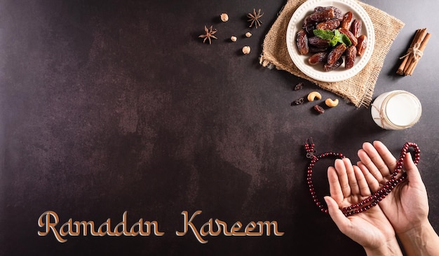 Concepto de fondo de Ramadán Kareem Manos sosteniendo un rosario con dátiles leche de frutas y el texto sobre fondo de piedra oscura