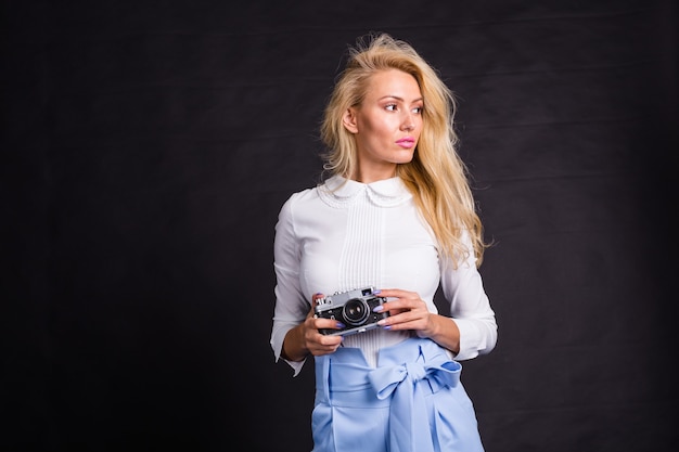 Concepto de fotografía, moda y personas: joven rubia haciendo una foto de algo y mirando algo cerca de ella sobre fondo negro con espacio de copia