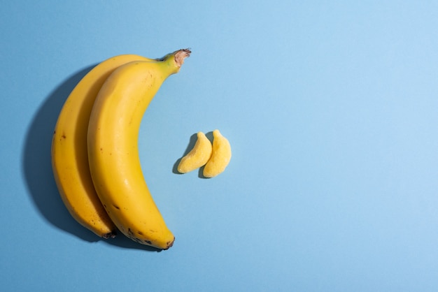 Concepto de fruta versus caramelo con plátanos en azul liso