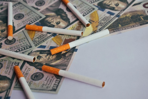 El concepto de fumar cigarrillos en el fondo del dólar Los cigarrillos esparcidos en los dólares