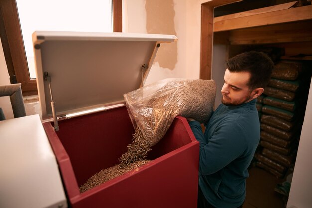 Concepto de futuro sostenible El hombre está cargando pellets de madera en una estufa de calefacción con una bolsa Calefacción doméstica en invierno