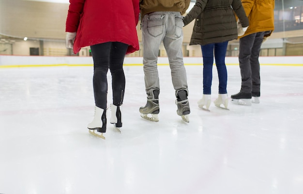 Foto concepto de gente, amistad, deporte y ocio - cerca de amigos felices patinando en la pista de hielo
