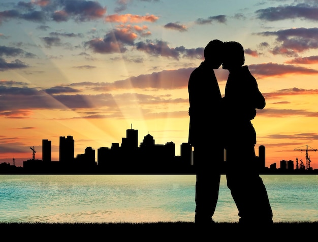 Concepto de gente gay. Silueta feliz beso gay en el mar al atardecer hermoso atardecer y la ciudad