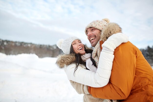 concepto de gente, temporada, amor y ocio - pareja feliz abrazándose y riéndose al aire libre en invierno