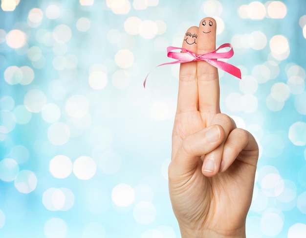 concepto de gesto, amor, vacaciones y partes del cuerpo - cierre de la mano con dos dedos atados por un nudo de lazo rosa sobre fondo azul de luces navideñas