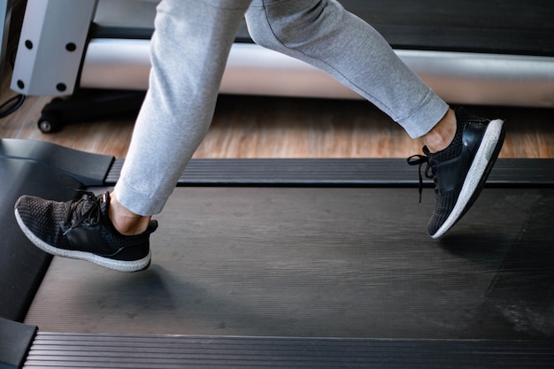 Concepto de gimnasio de entrenamiento un adolescente masculino con pantalones largos y zapatillas negras caminando en una cinta de correr para ejercicios cardiovasculares.