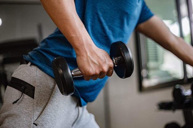 Concepto de gimnasio de entrenamiento un adulto joven con su brazo musculoso fuerte levantando una pesa hacia arriba y hacia abajo en el gimnasio.